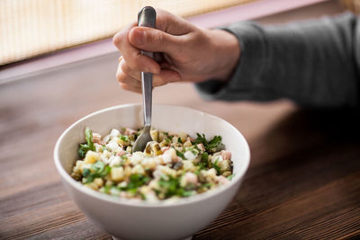 Close-up of hand holding salad in bowl on table