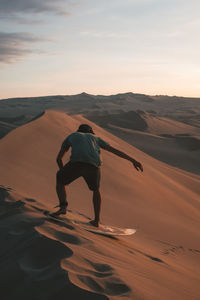 Rear view of man sandboarding at desert