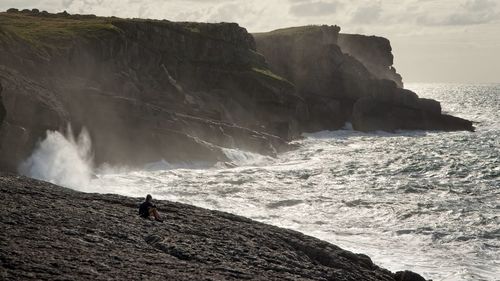 A couple contemplates the sea sitting on the rocks