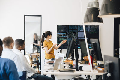 Female computer hacker presenting code on television screen during meeting with programmers in creative office