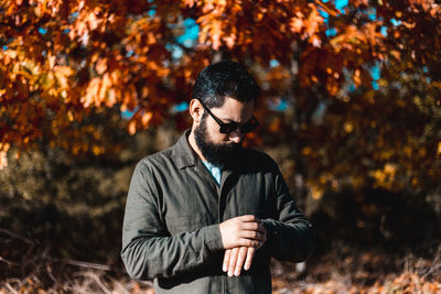 Young man looking away while standing on tree