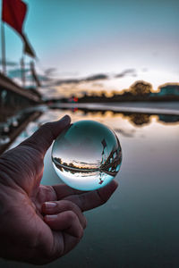 Close-up of hand holding crystal ball against sky