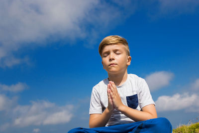 Low angle view of boy meditating sitting against sky