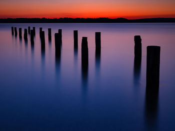 Wooden posts in sea against sky during sunset