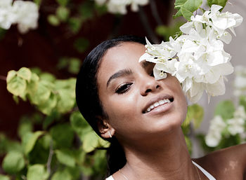 Close-up portrait of smiling young woman by white flowers