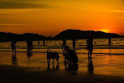 Silhouette people on beach against orange sky