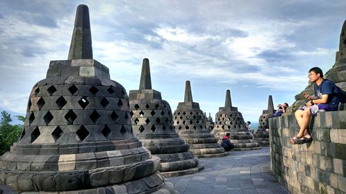 Man sitting on retaining wall at stupa against sky