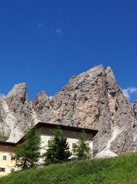 Low angle view of cottage on mountain against clear blue sky