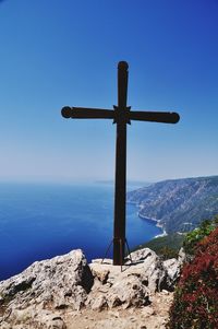 High angle view of cross on cliff by sea against clear blue sky