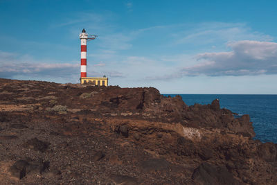 Lighthouse on rock by sea against sky