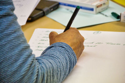 Cropped hand of man writing in paper on table