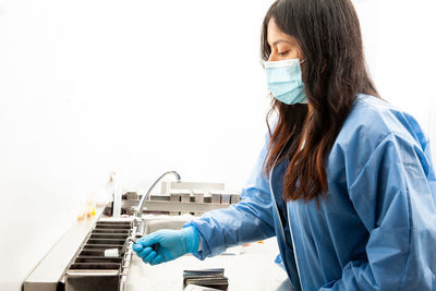 Side view of young woman wearing surgical mask against white background