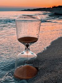 Close-up of wine glass on sand at beach during sunset