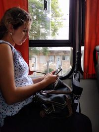 Woman using mobile phone while sitting on window