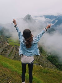Rear view of woman with arms raised against mountains