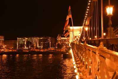 Illuminated bridge over river by buildings in city at night