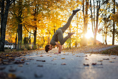 Side view of man doing handstand on road during autumn