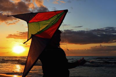 Silhouette of man holding kite while standing on beach