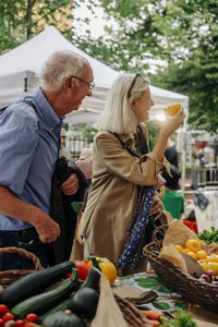 Senior woman examining persimmon while standing by man at market