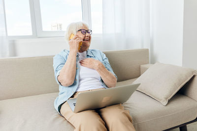 Young woman using phone while sitting on sofa at home