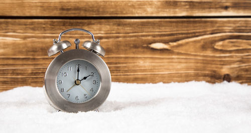 Close-up of alarm clock on snow against wooden wall