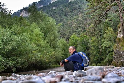 Man looking away while sitting against trees at forest