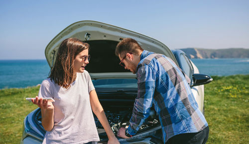 Young couple repairing car at beach