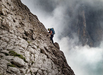 Low angle view of woman climbing on mountain against sky