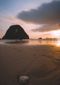 Full length of woman standing on beach against sky during sunset