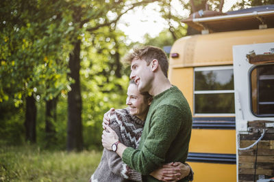 Smiling mid adult couple embracing while enjoying camping in forest