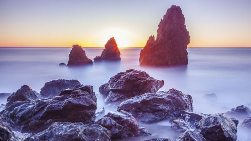 Rocks in sea against sky during sunset