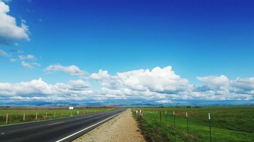 Road amidst field against blue sky