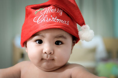 Close-up portrait of cute shirtless baby boy wearing santa hat
