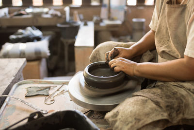 Midsection of potter making pot on wheel at workshop