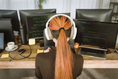 Rear view of female programmer working on laptop in creative office