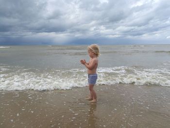 Full length of shirtless boy on beach against sky