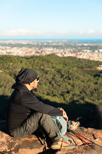 Side view of woman sitting on rock against sky