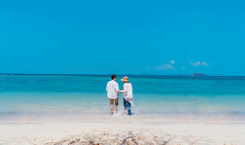 Rear view of couple standing at beach against sky