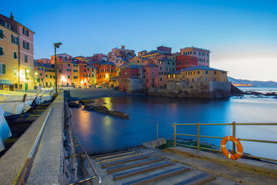 Buildings by river against sky in city at dusk