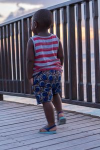 Rear view of boy walking on footbridge by railing