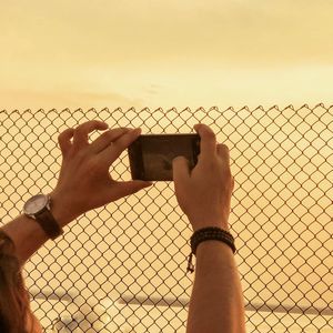 Low section of man using mobile phone against sky