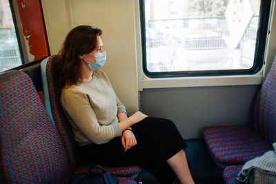 Young woman wearing medical mask while sitting in transport