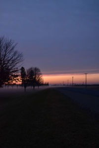 Silhouette bare trees on road against clear sky at sunset