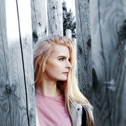 Young woman looking away while standing by tree trunks