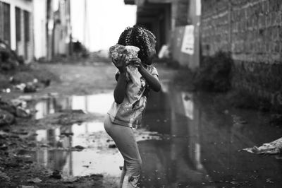 Side view of girl throwing stone while standing on wet street