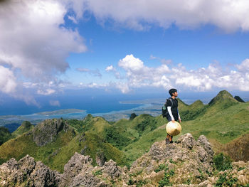 Side view of man standing on mountain peak against cloudy sky