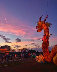 Low angle view of dragon and woman against sky at sunset