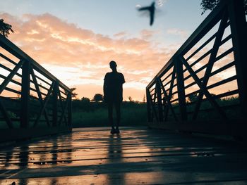 Silhouette man standing on footbridge against sky