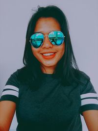 Portrait of smiling woman wearing sunglasses against white wall