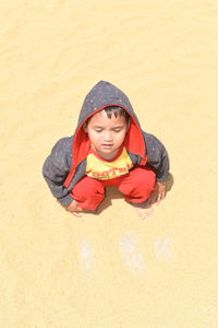 High angle view of boy crouching on sand at beach